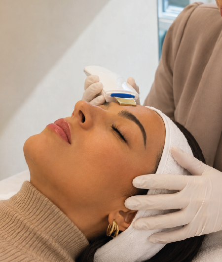 Esteticista usando luvas aplicando aparelho de peeling ultrassônico na testa de uma cliente deitada, durante sessão de limpeza de pele premium em Curitiba.